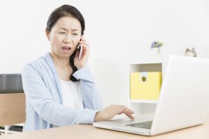パソコンを操作しながら電話している女性